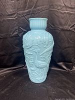 Front view of blue milk glass vase embossed with bird designs on a black background.