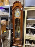 Full view of tall colonial wooden grandfather clock with glass panel showing pendulum and weights.