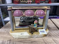 Front view of sculpture showing clown figure holding luggage cart, Corvette behind glass with "CORVETTE" lettering, signed on marble base.