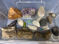 Top down view of grouping of crystals and rocks including amethyst cluster, quartz points, and various other mineral specimens in plastic bin.