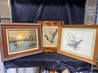 Grouping of three duck themed artworks on display with black fabric background.