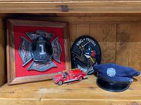 Photo showing Runnymede fire department plaque, King of Prussia metal plaque, Franklin Mint fire truck model, and Radnor fire uniform hat on wooden shelf.