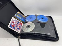 Black zippered binder partially open showing several CD sleeves with CDs and pamphlets visible, branded Fellowes