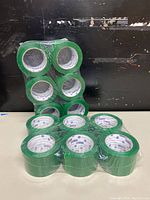 Twelve rolls of green packaging tape, shrink-wrapped together in a black background setting.