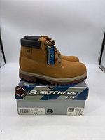 Side view of tan Skechers waterproof boots on top of their blue and gray Skechers USA box showing waterproof label and padded collar.