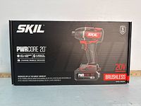 Front view of the Skil PWRCore 20V Impact Driver Kit box showing branding and key features including 20V brushless motor, 25% longer run time, 5-minute charging, and mobile device charging capability.