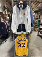 Photo showing white and black Nike Air Jordan sweat jacket hanging above yellow Lakers basketball jersey with number 32.