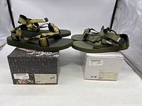 Two pairs of olive green Suicoke sandals shown on their respective boxes, presenting different strap designs and very light wear.