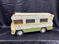 Side view of rusty vintage metal toy RV with white and green paint and translucent plastic windows.