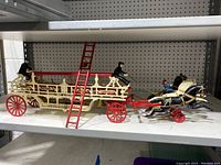 Side view showing entire length of vintage cast iron horse drawn hook ladder fire engine with three horses and two ladders.
