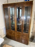Front view of the 1970s Founders illuminated display cabinet showing four glass doors with wood veneer lower panels and brass trim along the edges.