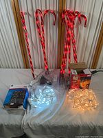 Six red and white striped candy cane LED sticks standing against a wall with boxes and clear string lights lying in front