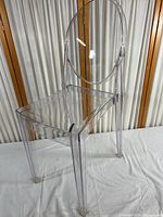 Clear plexiglass chair showing front perspective, displaying seat, legs, and oval backrest.