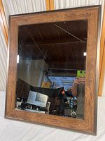 Full view of the mirror showing the reflective glass and composite wood frame with wood grain pattern.