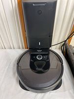 Robot vacuum iRobot Roomba i7 docked in clean base station on a white surface with power cord visible.