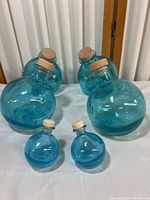 Full view of six Ocean Vodka empty blue glass globe containers with cork stoppers. Four larger, two smaller, arranged on a table.