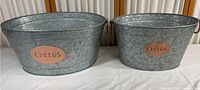 Pair of galvanized metal ice/party buckets side by side showing copper 'CHEERS' plaques on front and copper handles on sides