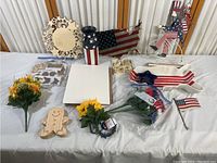 Full view of patriotic and floral items laid out on white tablecloth including wooden decorations, ceramic plates, and faux flowers.