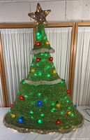 Artificial Christmas tree decoration showing bottom and top segments with lights and star topper against a wall