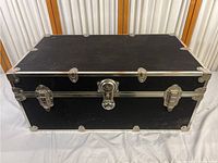 Closed view of black Rhino trunk with metal corner protectors and three latch locks on front.