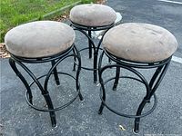 Three round stools with black metal frames and beige fabric seats showing wear placed outdoors on pavement.