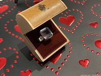 Ring displayed in a wooden box on red heart-patterned mat