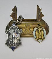 View of 1939 CNE sterling silver and enamel watch fob medallion with chain alongside 1929 enamel medal placed on coronation display stand