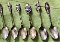 Photo showing six sterling silver souvenir spoons with intricate handles and embossed bowls, including a spoon with a trillium design and one with a bent bowl from Moose Jaw.