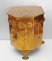 Front angled view of hexagonal copper coal scuttle showing embossed bow and drop motifs on panels, cloven paw feet