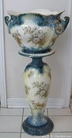 Full front view of the antique Stoke on Trent jardiniere placed on matching pedestal stand, showing floral and embossed details.