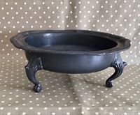 Side view of antique oval pewter fruit bowl with visible scalloped edges and three ornate feet supporting the bowl on a polka dot cloth surface.