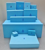 Photo shows 11 blue vintage Birks boxes of various sizes with the Birks logo on top arranged on a flat surface.