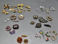 Overview image showing a large assortment of vintage brooches laid out on a flat surface, featuring different styles and colors including gold, silver, amber, and multicolored rhinestones.