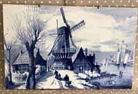 Front of large blue and white Dutch ceramic wall tile showing windmill, houses, figures, trees, and boats.