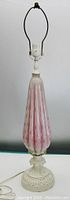 Full view of the lamp showing height, harp, and shape of pink glass body with white painted metal base and neck.