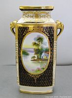 Front view of Nippon vase showing hand painted landscape with house and trees on black and gold background and elephant handle