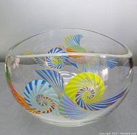 Front view of clear glass bowl with colorful abstract spiral and fan design.