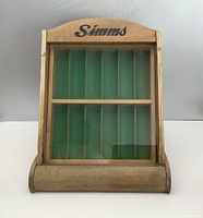 Front view of the wooden slant front store counter display case branded with Simms showing glass front and green felt compartments inside