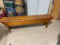 Front view of a vintage solid pine wood bench showing its sturdy single board seat, rounded edges, and side skirts.