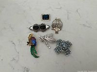 Seven brooches arranged on a neutral surface showing full group including sterling and costume brooches