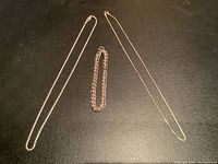 Three sterling silver pieces on black surface: two necklaces and one bracelet.