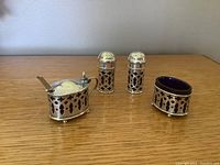 Full shot of the salt cellar, mustard pot with spoon, and salt & pepper shakers showing silver bodies with cut-out detailing and cobalt blue glass inside.