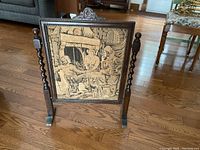 Full view of tapestry fireplace screen showing the tapestry and the full wooden frame with twist sides and carved floral crest on top.