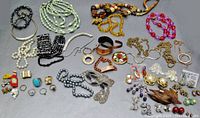 Full view of assorted vintage costume jewelry including necklaces, bracelets, rings, earrings and brooches laid out on gray surface