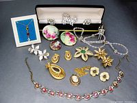 Wide view of entire lot showing all jewellery pieces including floral brooches, cameo pendant, rhinestone set, bead necklace, gold-tone floral pieces, earrings, and presentation boxes.