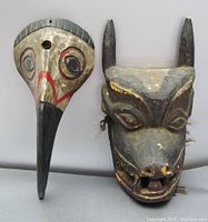Two carved wooden masks side by side on a flat surface, showing front details and size comparison.