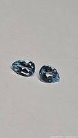 Pair of pear shaped sky blue topaz gemstones photographed closely on a white/light background to show color, size and cut.