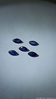 Top-down photo of five marquis cut denim blue sapphires on white background showing stone shape, size, and color.