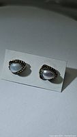 Pair of teardrop-shaped mother of pearl earrings set in ornate 925 sterling silver with a slight patina, displayed on a white card.
