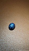 Close-up image showing natural blue star sapphire with visible 6-ray star asterism on surface, placed on textured brown background.